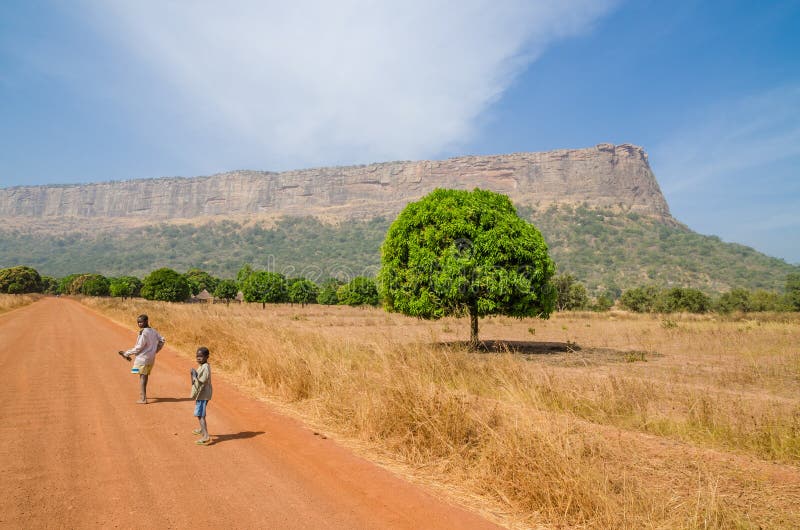 Labe, Guinea - December 20, 2013: Two unidentified boys walking on dirt road looking back with tree and mountain