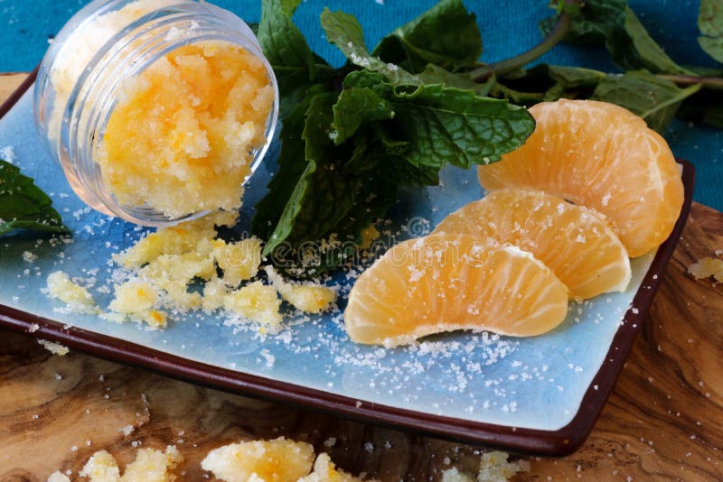 Mandarin orange lip and body scrub and mint leaves on a beautiful olive wood board. Mandarin orange lip and body scrub and mint leaves on a beautiful olive wood board.