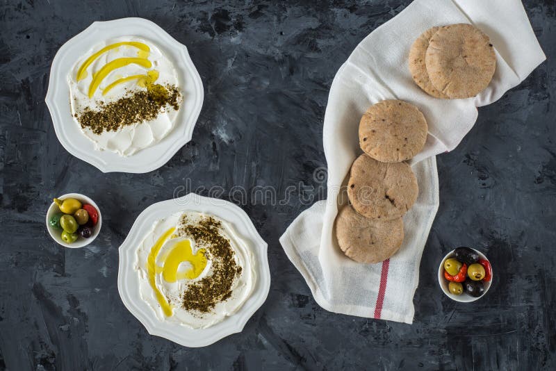 Labneh labaneh middle eastern soft white goat`s milk cheese with olive oil ,olives , za`atar , lemon, with pita bread over blac