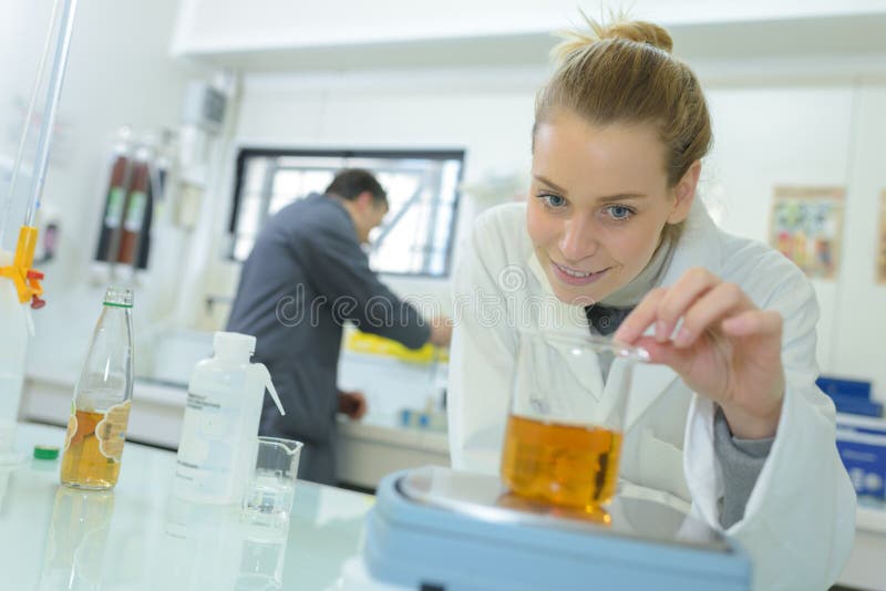 Laboratory technician weighing glass flask containing liquid