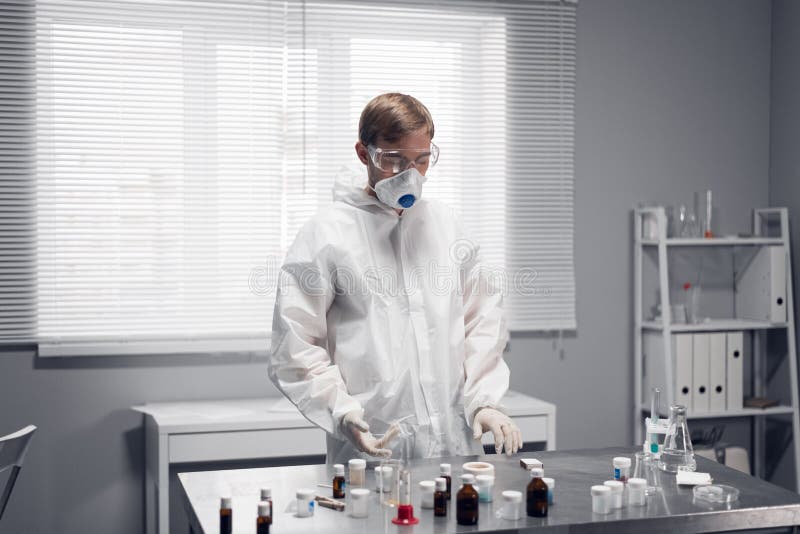 Laboratory worker in a protective mask and overalls carrying out an experiment stock photos