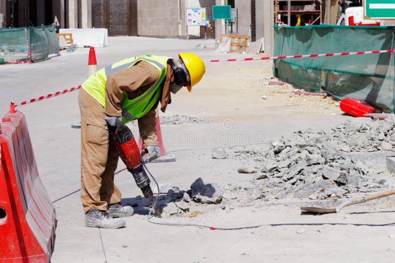 A laborer is well protected in safety gear as he uses a jackhammer to break up a reinforced concrete pavement. A laborer is well protected in safety gear as he uses a jackhammer to break up a reinforced concrete pavement