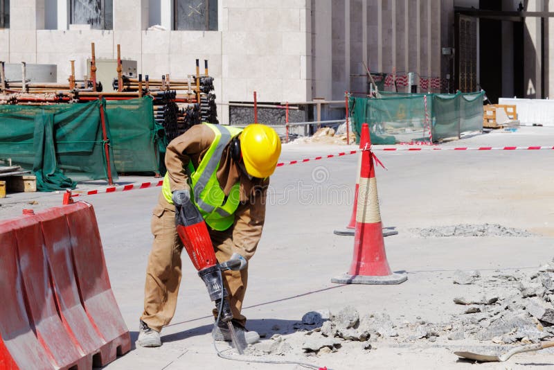 A laborer is well protected in safety gear as he uses a jackhammer to break up a reinforced concrete pavement. A laborer is well protected in safety gear as he uses a jackhammer to break up a reinforced concrete pavement