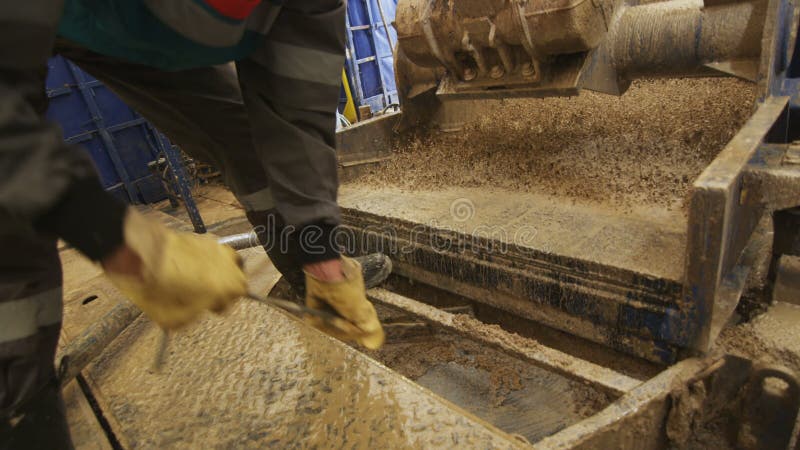 Laborer w gumowych butach grabije w górę skał w bagrownicy maszynie