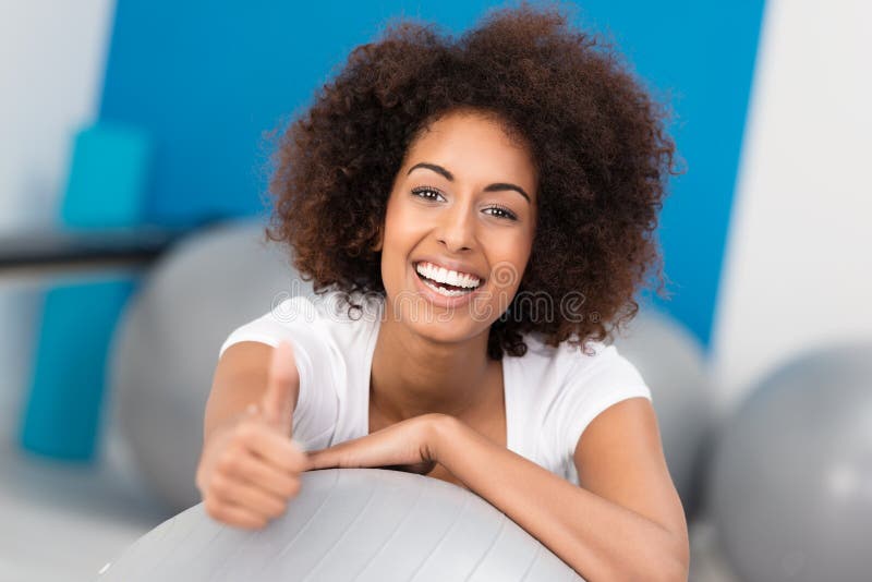 Laughing attractive African American woman with a wild afro hairstyle working out in a gym giving a thumbs up gesture of approval. Laughing attractive African American woman with a wild afro hairstyle working out in a gym giving a thumbs up gesture of approval