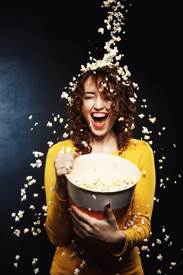 Lachende junge Frau, die unter käsiger Popcorndusche am Kino bleibt lizenzfreie stockfotos Lachende junge Frau, die unter käsiger Popcorndusche am Kino bleibt lizenzfreie stockfotos