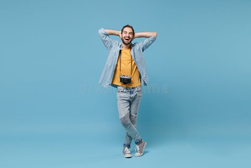 Laughing traveler tourist man in summer casual clothes with photo camera isolated on blue background. Male passenger traveling abroad on weekends. Air flight journey concept. Hold hands behind head. Laughing traveler tourist man in summer casual clothes with photo camera isolated on blue background. Male passenger traveling abroad on weekends. Air flight journey concept. Hold hands behind head