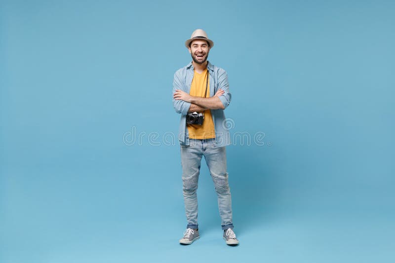 Laughing traveler tourist man in yellow casual clothes with photo camera isolated on blue background. Male passenger traveling abroad on weekends. Air flight journey concept. Holding hands crossed. Laughing traveler tourist man in yellow casual clothes with photo camera isolated on blue background. Male passenger traveling abroad on weekends. Air flight journey concept. Holding hands crossed