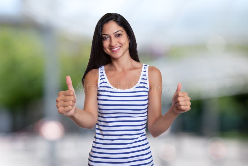 Lachende Turkse vrouw in een de zomeroverhemd die beide duimen tonen stock foto Lachende Turkse vrouw in een de zomeroverhemd die beide duimen tonen stock foto