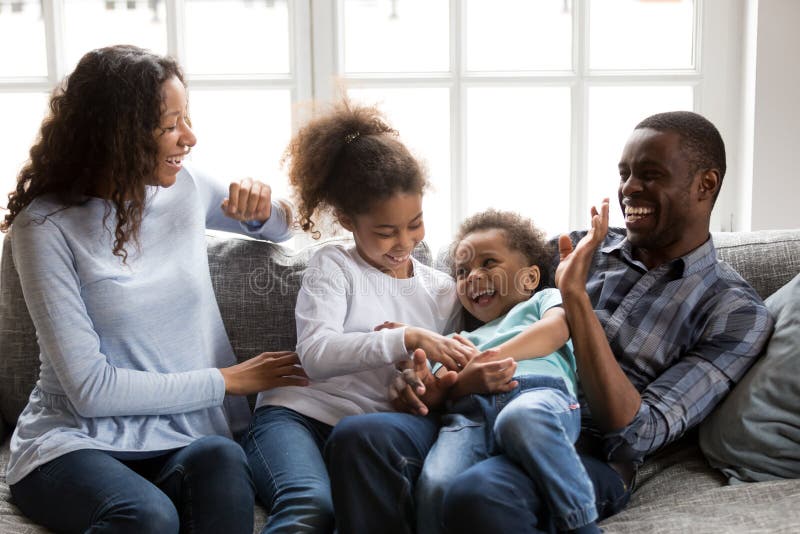 Lachendes Spielen der glücklichen schwarzen Familie, Kinder zu Hause kitzelnd stockfotos