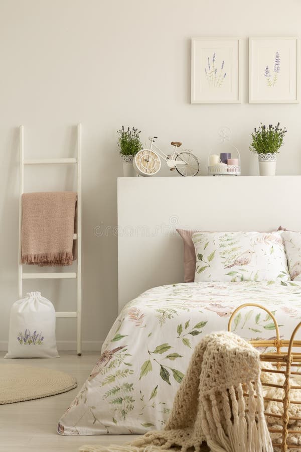 Ladder with pink blanket next to bed in feminine bedroom interior with lavender flowers and posters. Real photo concept