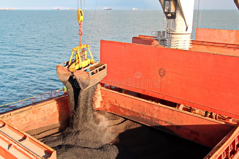 Loading coal from cargo barges onto a bulk carrier using ship cranes and grabs at the port of Samarinda, Indonesia. View of a close-up of the work of bulldozers and loaders. Loading coal from cargo barges onto a bulk carrier using ship cranes and grabs at the port of Samarinda, Indonesia. View of a close-up of the work of bulldozers and loaders.