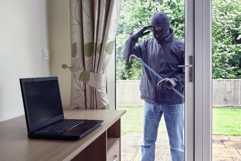 Thief breaking into a house via a patio doors window with a crowbar to steal a laptop computer from an office desk. Thief breaking into a house via a patio doors window with a crowbar to steal a laptop computer from an office desk
