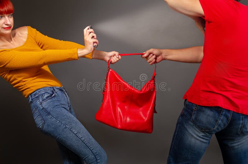 A girl defending pepper spray from a robber who is trying to take away her bag. A girl defending pepper spray from a robber who is trying to take away her bag