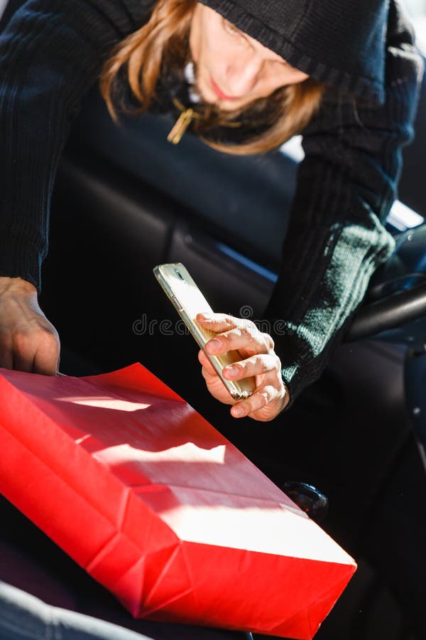 Ladro dello scassinatore che ruba smartphone e borsa dall'automobile fotografia stock Ladro dello scassinatore che ruba smartphone e borsa dall'automobile fotografia stock