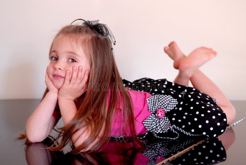 A beautiful little girl with her head propped in her hands. She's wearing a pink and black polka dot dress with a checked bow and a pink lady bug on it. She look's as if she's thinking and has her legs crossed and is barefoot. She's posed on a baby grand piano. A beautiful little girl with her head propped in her hands. She's wearing a pink and black polka dot dress with a checked bow and a pink lady bug on it. She look's as if she's thinking and has her legs crossed and is barefoot. She's posed on a baby grand piano