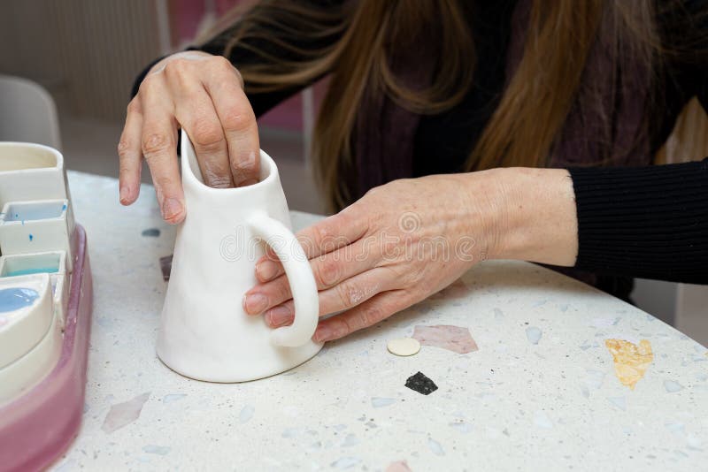 lady cleans white pitcher with sandpaper before applying pattern to clay milk jug in workshop royalty free stock images