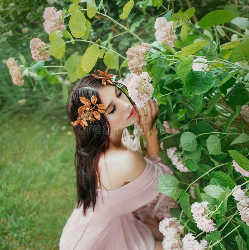 Lady with dark black hair in a lovely sweet pink peach dress sits in flowers