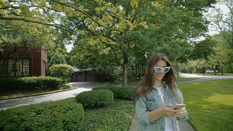 Lady in funny green eyeglasses walks in park and chats on cell phone.