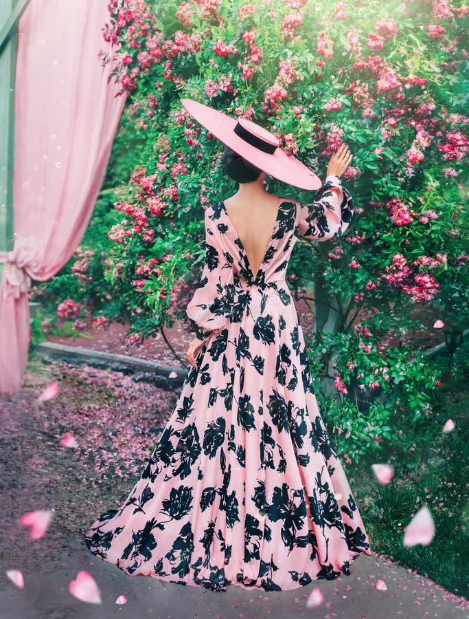 Lady in long pink dress with black patterns. Woman in the last thing in hats