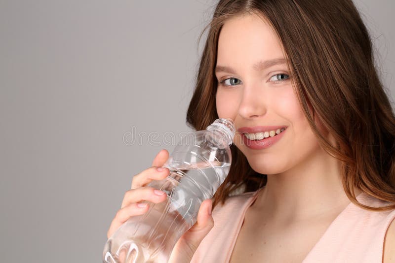 Lady in pink top with bottle of water. Close up. Gray background