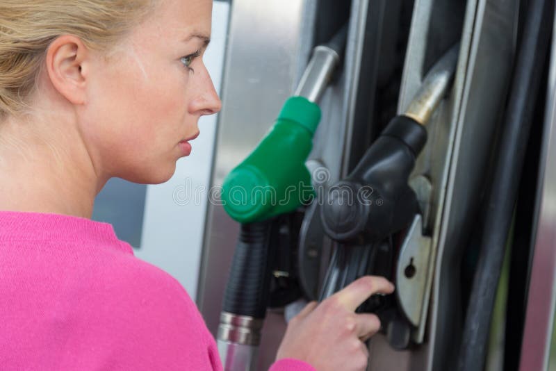 Lady pumping gasoline fuel in car at gas station.