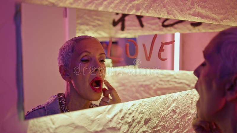 Lady reflection touching face lips in neon bathroom closeup. Word love on mirror stock photo