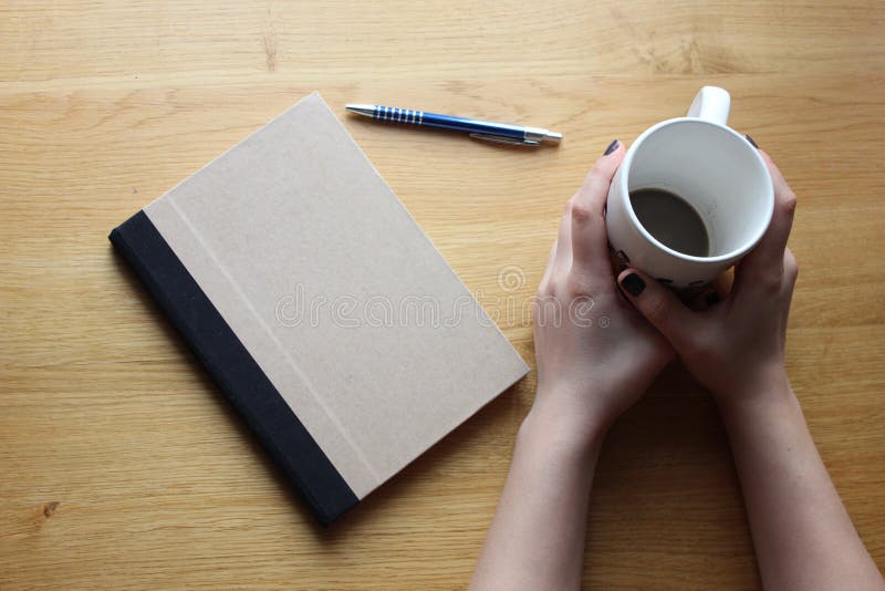 Lady s hands with cofee cup, notebook and pen on the table