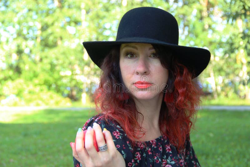 lady treats Apple. woman in a black dress and hat, with red curly hair, holds out her hand and offers an Apple stock images lady treats Apple. woman in a black dress and hat, with red curly hair, holds out her hand and offers an Apple stock images