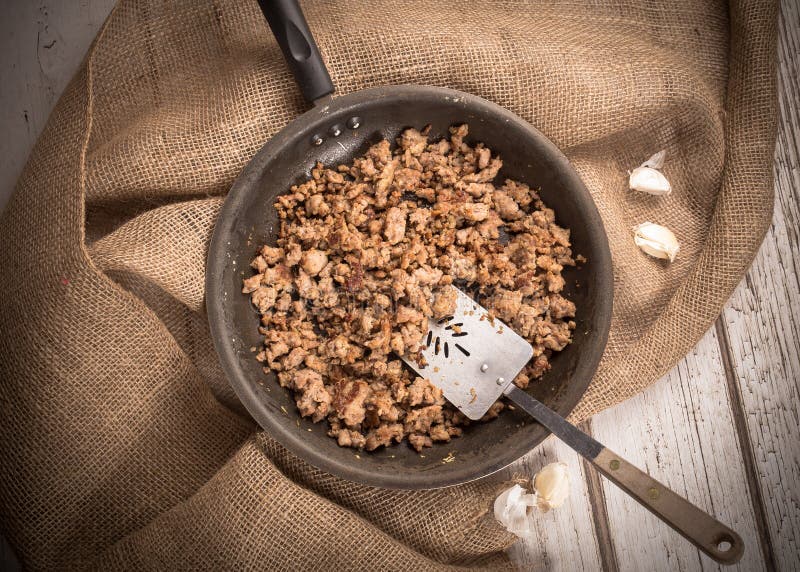 Cooking Ground sausage meat in frying pan with garlic and burlap background. Cooking Ground sausage meat in frying pan with garlic and burlap background