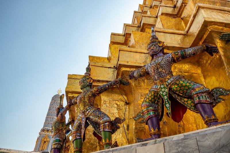 Lage hoek van reuzestandbeelden op de basis van gouden pagode in koninklijke tempel in groot paleis met duidelijke blauwe hemelac stock foto Lage hoek van reuzestandbeelden op de basis van gouden pagode in koninklijke tempel in groot paleis met duidelijke blauwe hemelac stock foto