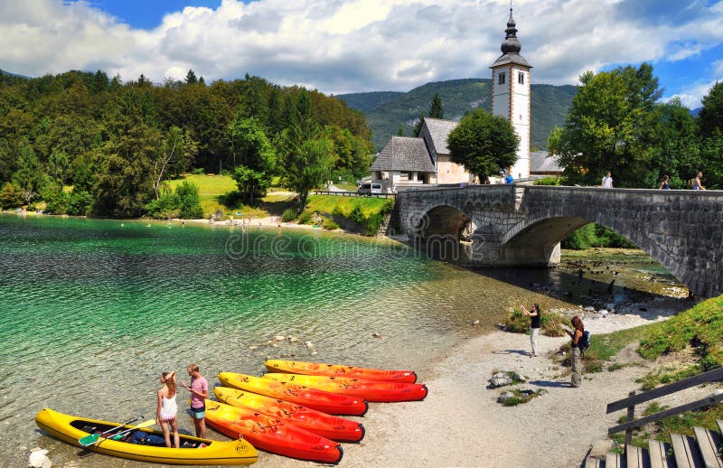Lago Bohinj com barcos e turistas, igreja de St John o batista com ponte Parque nacional de Triglav, Eslovênia fotografia de stock Lago Bohinj com barcos e turistas, igreja de St John o batista com ponte Parque nacional de Triglav, Eslovênia fotografia de stock