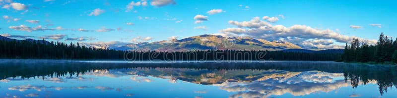 Panorama of morning sun and low clouds over the Rocky Mountains at Annette Lake in Jasper National Park with reflections of Majestic Mountain, Aquila Mountain, Mount Edith Cavell on the calm waters. Panorama of morning sun and low clouds over the Rocky Mountains at Annette Lake in Jasper National Park with reflections of Majestic Mountain, Aquila Mountain, Mount Edith Cavell on the calm waters.