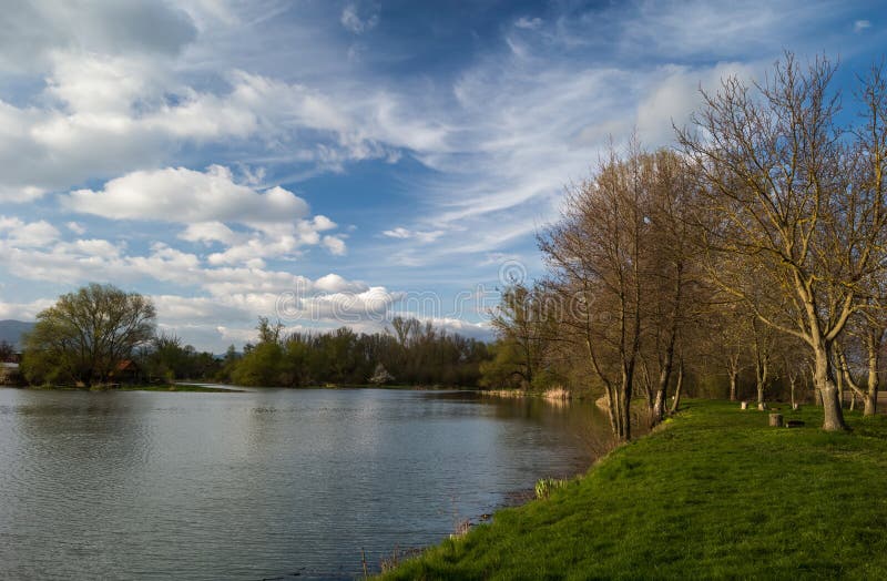 Spring landscape, lake with beautiful blue sky and white clouds. Side light before sunset