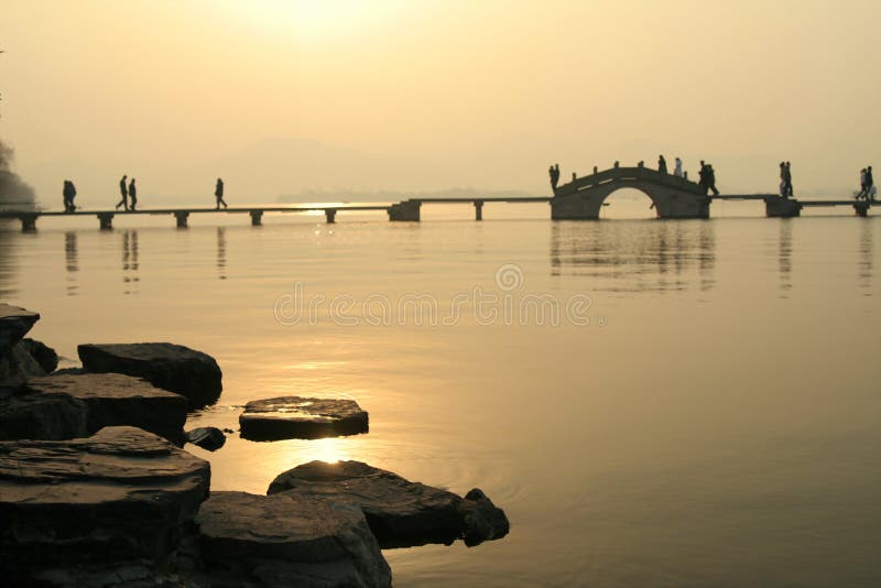 Sunset view over West Lake, China with people walking across a bridge. Sunset view over West Lake, China with people walking across a bridge.