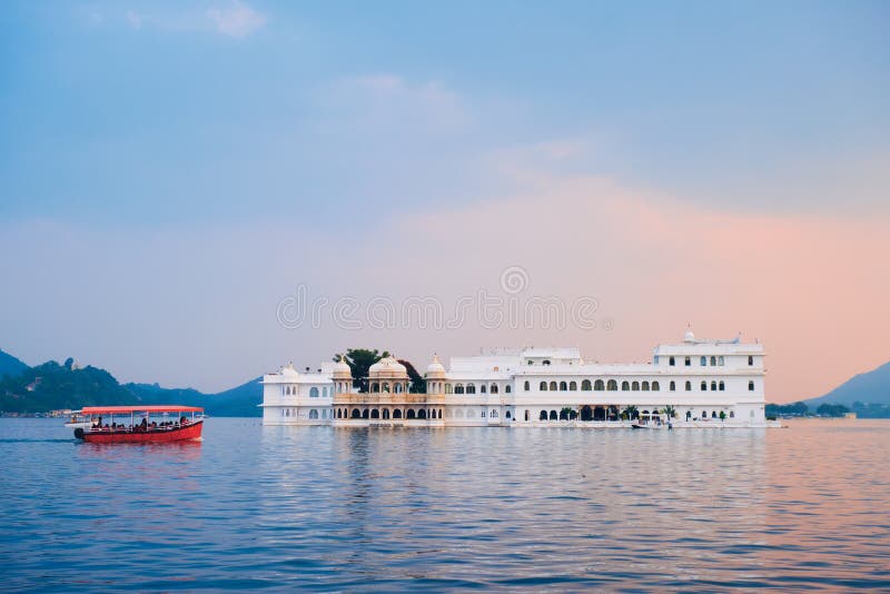 Romantic luxury India travel tourism - tourist boat in front of Lake Palace Jag Niwas complex on Lake Pichola on sunset with dramatic sky, Udaipur, Rajasthan, India. Romantic luxury India travel tourism - tourist boat in front of Lake Palace Jag Niwas complex on Lake Pichola on sunset with dramatic sky, Udaipur, Rajasthan, India