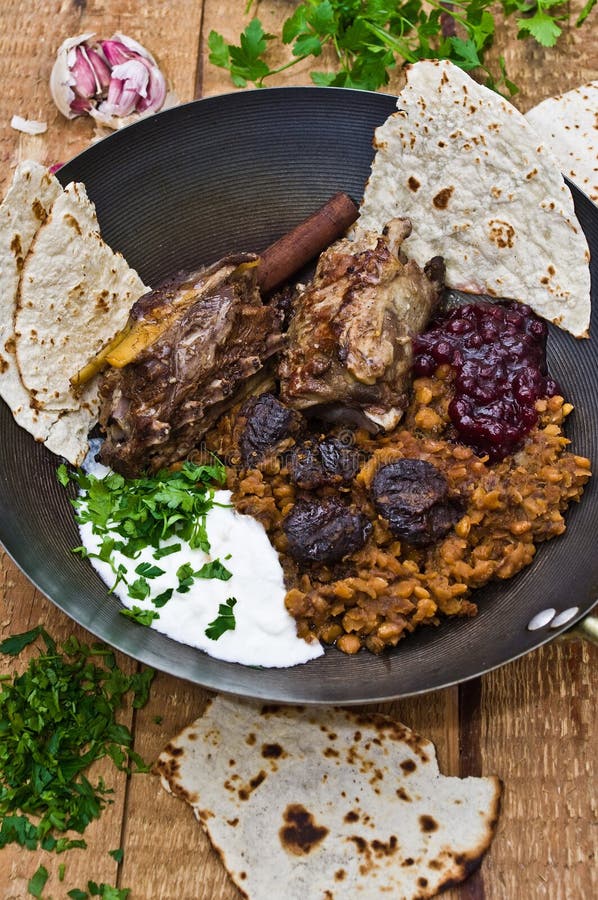 Lamb meal. Lamb loin with yellow peas and prunes in a frying pan, on a wooden board. The dressing is a seasoned yogurt from Middle East. Served with plain pita royalty free stock photos Lamb meal. Lamb loin with yellow peas and prunes in a frying pan, on a wooden board. The dressing is a seasoned yogurt from Middle East. Served with plain pita royalty free stock photos