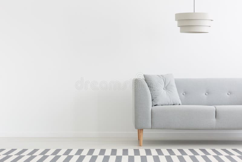Grey couch in white minimal apartment interior with copy space on empty wall. Real photo stock image