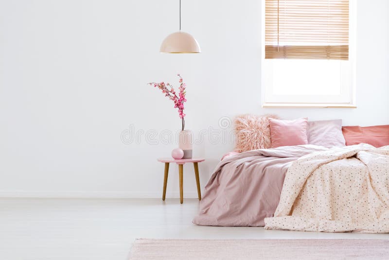 Lamp above table with flowers in pink pastel bedroom interior wi