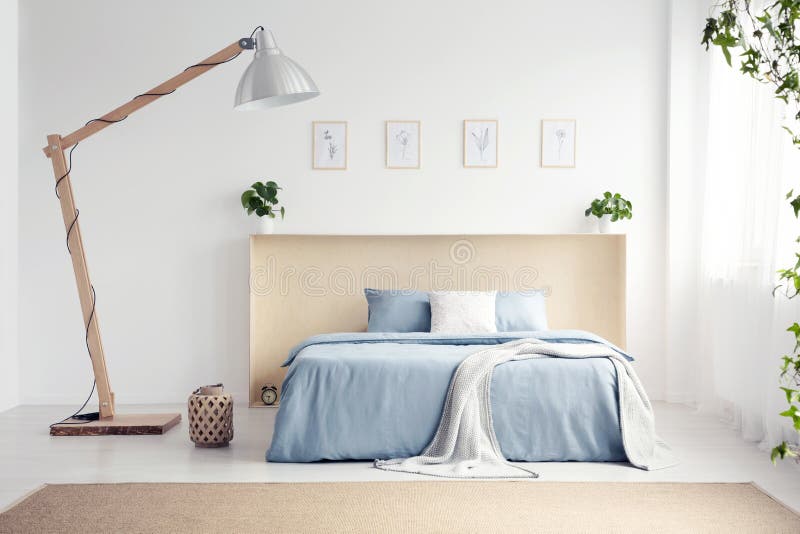 Lampe de concepteur à côté de lit bleu avec la couverture dans la chambre à coucher blanche international image libre de droits Lampe de concepteur à côté de lit bleu avec la couverture dans la chambre à coucher blanche international image libre de droits