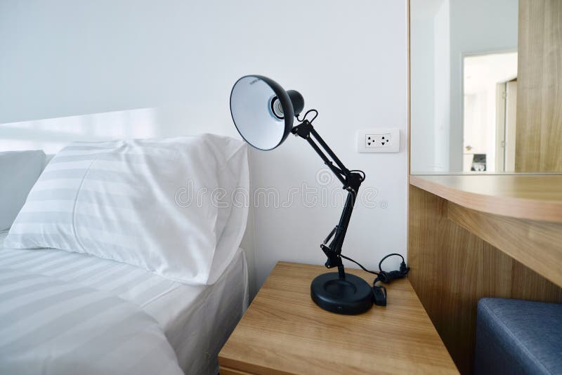 Lampe moderne sur le nightstand en bois dans la chambre à coucher moderne blanche, interi photographie stock Lampe moderne sur le nightstand en bois dans la chambre à coucher moderne blanche, interi photographie stock