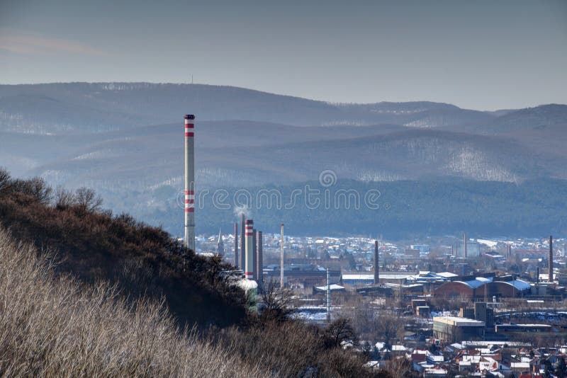 Winter cityscape with tall chimneys and industrial buildings in Diosgyor Vasgyar district of Miskolc with forested Bukk Mountains of North Hungarian Mountain Range, Hungary Eastern / Central Europe. Winter cityscape with tall chimneys and industrial buildings in Diosgyor Vasgyar district of Miskolc with forested Bukk Mountains of North Hungarian Mountain Range, Hungary Eastern / Central Europe