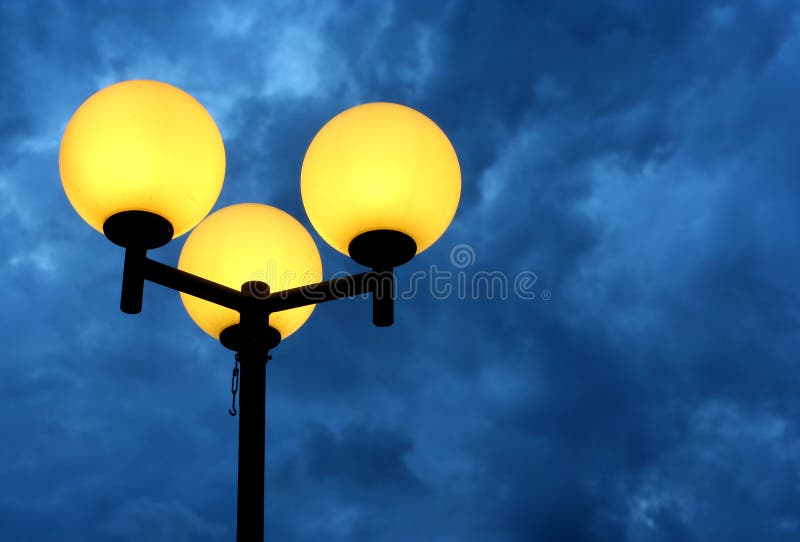 A burning streetlight with three bulbs at dusk. A burning streetlight with three bulbs at dusk