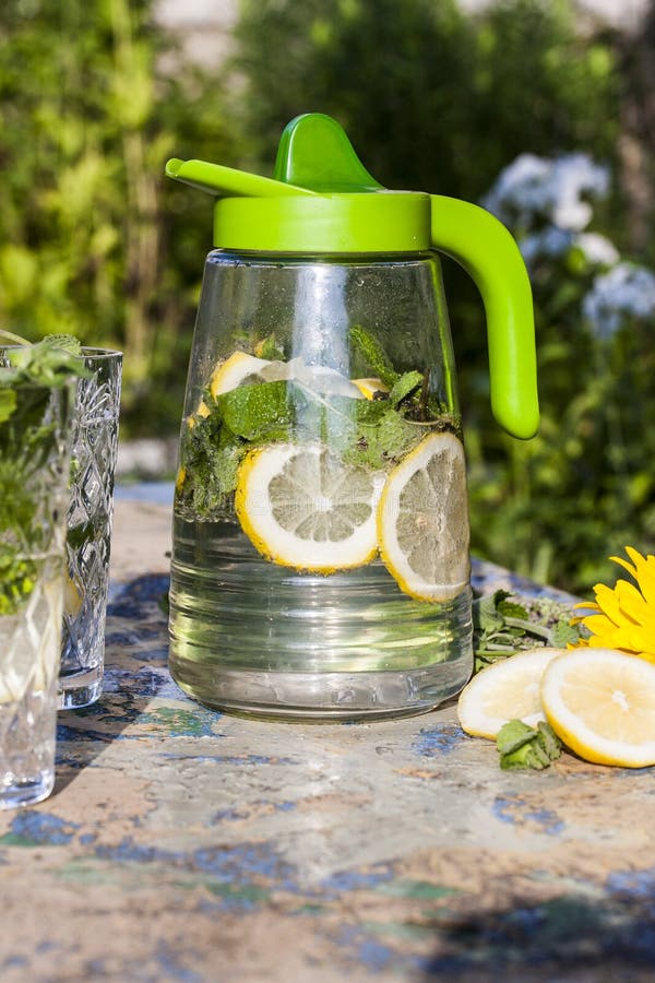 Lanciatore della limonata con il limone e la menta sulla tavola del giardino fotografia stock Lanciatore della limonata con il limone e la menta sulla tavola del giardino fotografia stock