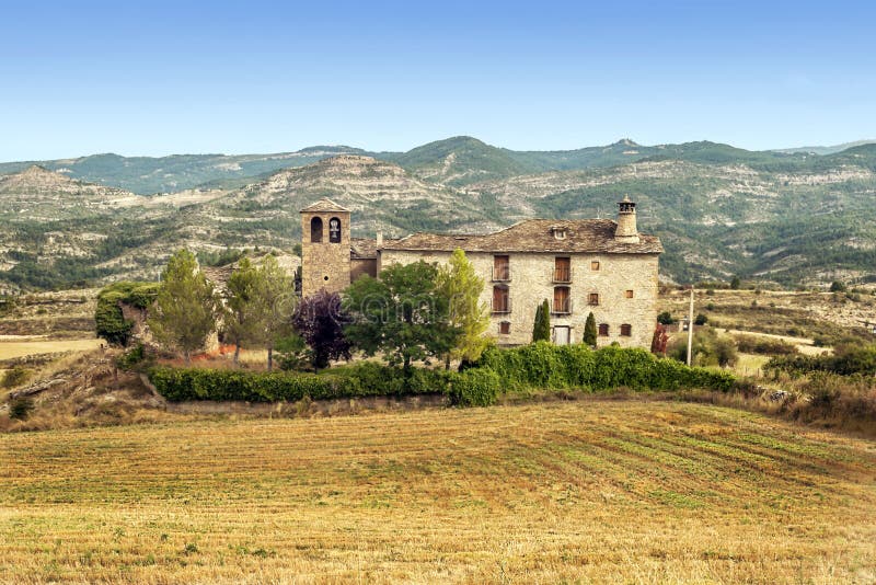 Rural house with a bell tower on one side and the other a chimney, is a stone house with a colorful trees surrounded by wheat fields and mountains in the background on a clear day. Rural house with a bell tower on one side and the other a chimney, is a stone house with a colorful trees surrounded by wheat fields and mountains in the background on a clear day