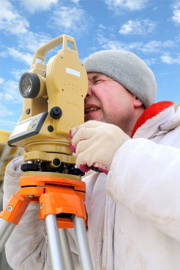 Land surveyor working with theodolite equipment at a construction site in winter over blue sky. Land surveyor working with theodolite equipment at a construction site in winter over blue sky