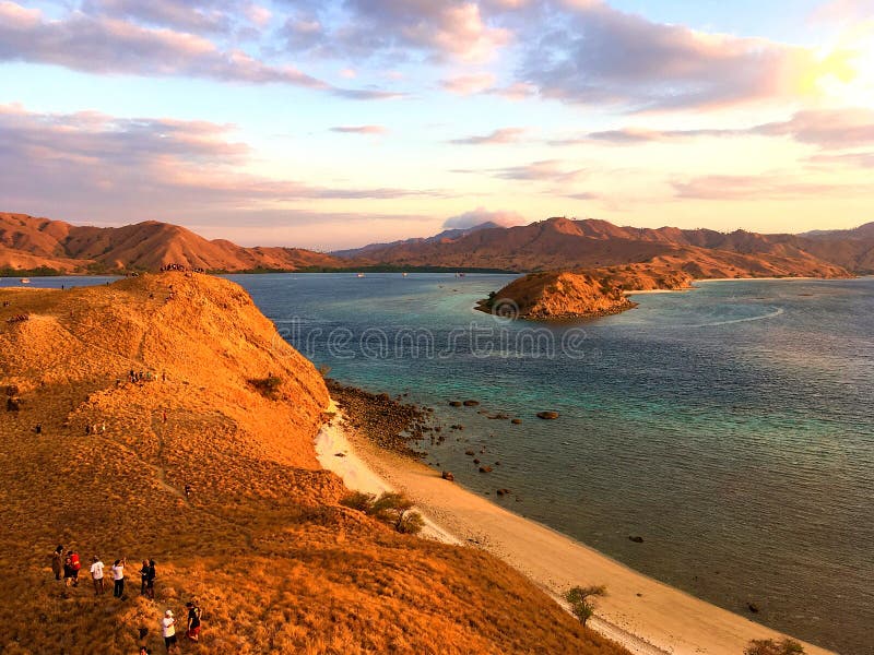 Landmark view of `GILI LAWA DARAT` with green savanna grass and blue sea in an evening, Komodo Island