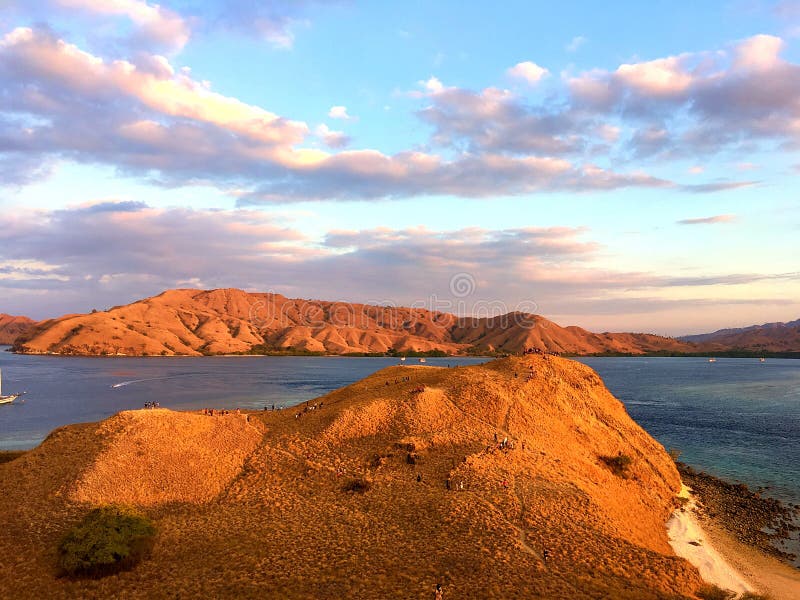 Landmark view of `GILI LAWA DARAT` with green savanna grass and blue sea in an evening, Komodo Island