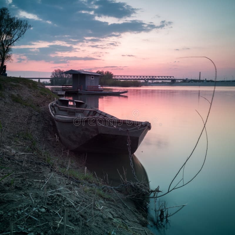 Landscape scenic view of nature of Sava river with old used fishing boat moored along coast to willow stump framed with branch or