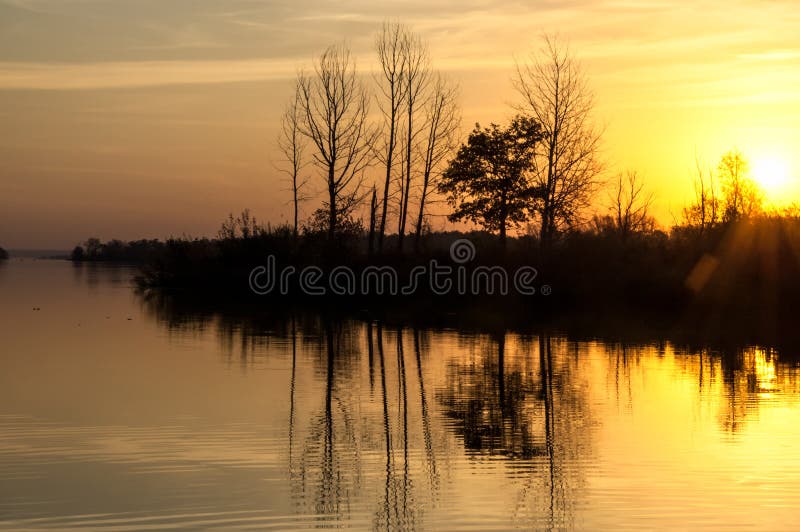 Landscape. Sunset over the lake, fall trees reflected in water.